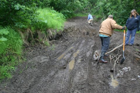 2003 Jeep TJ - People work on a muddy, rutted trail in a wooded area.