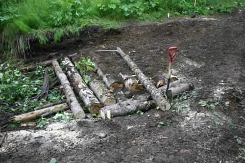 2003 Jeep TJ - Logs are arranged on the ground, possibly for a trail repair, with a shovel stuck in the dirt nearby.