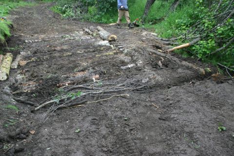2003 Jeep TJ - Logs are placed on a muddy trail, likely for reinforcement or repair, with a person visible in the distance.