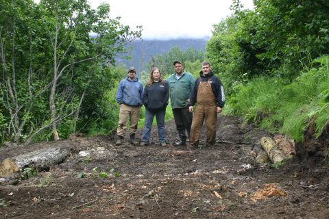 2003 Jeep TJ - Four individuals pose for a photo on a rough, muddy trail surrounded by dense foliage and trees.