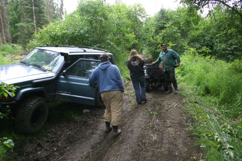 2003 Jeep TJ - People gathered around a Jeep Cherokee XJ and an ATV on a muddy trail in a wooded area.