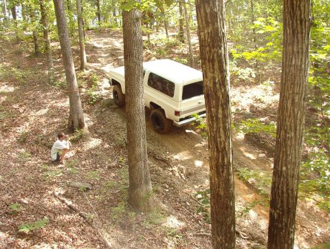 1983 Ford Bronco - White Chevrolet K5 Blazer navigates a dirt path through a forest.