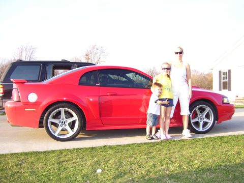 2004 Ford Mustang - A family poses with their red 2004 Ford Mustang coupe, captured in a side profile shot.