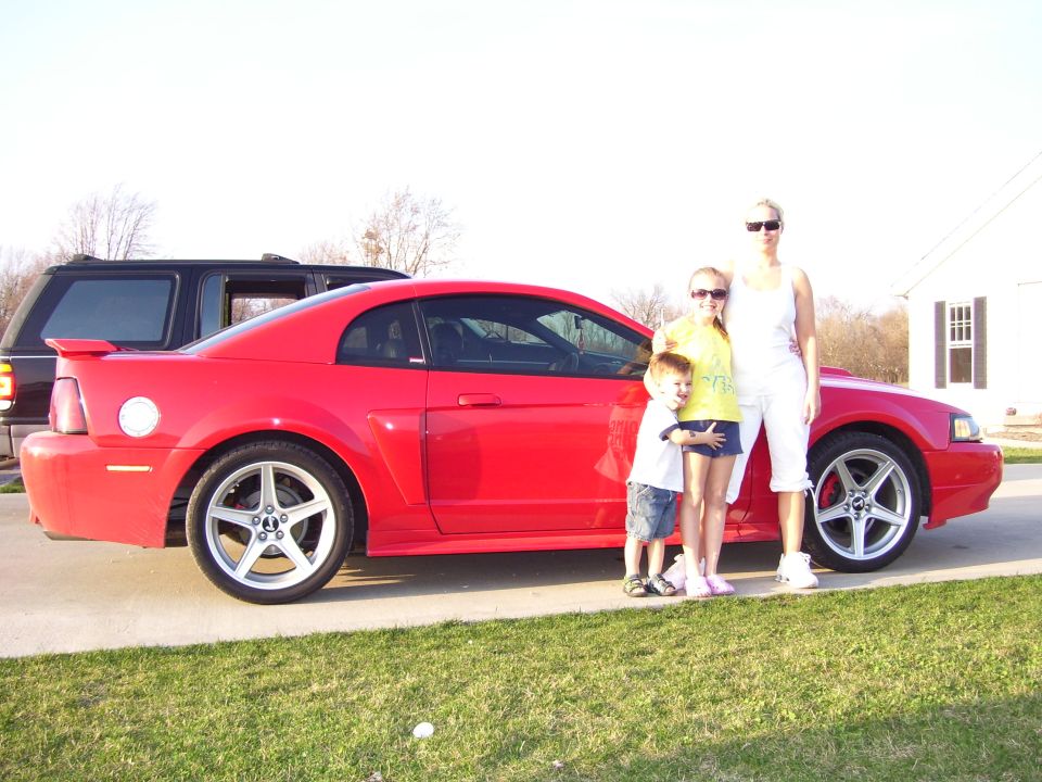 Red 2004 Ford Mustang coupe, side view, with a family posing