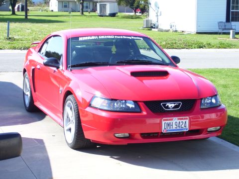 2004 Ford Mustang - A red 2004 Ford Mustang is parked in front of a residential house on a sunny day.