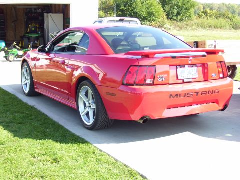 2004 Ford Mustang - Rear view of a red 2004 Ford Mustang GT parked in a driveway, a custom spoiler and aftermarket wheels.