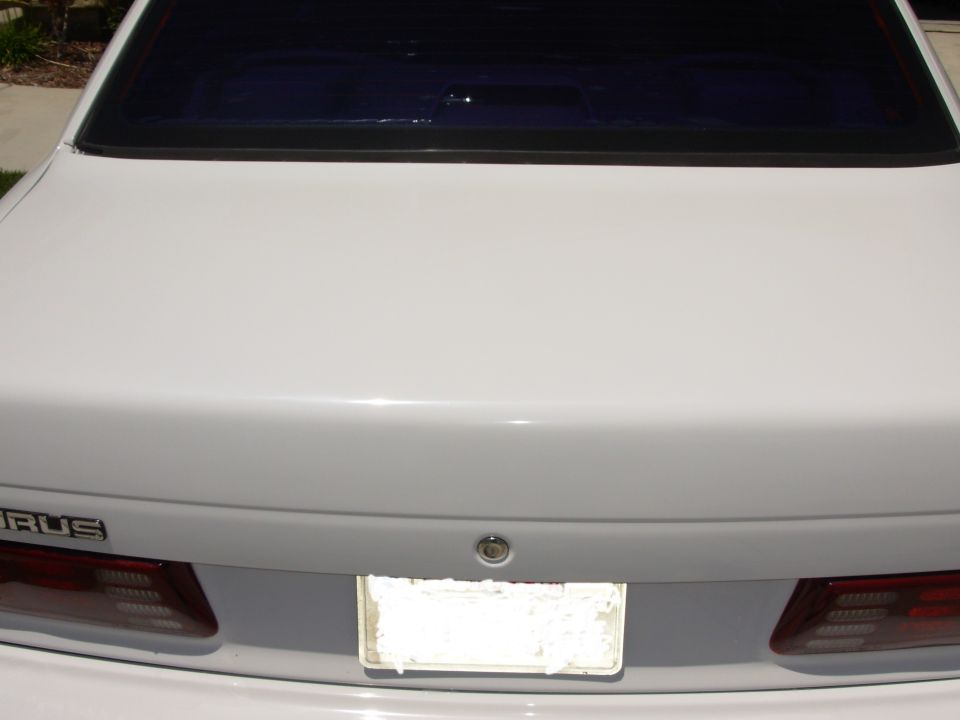 Rear of a white sedan showing the trunk lid, taillights, and a license plate area. The word 'URUS' is visible on the trunk