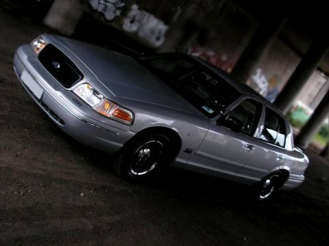 1998 Ford Crown Victoria - A silver 1998 Ford Crown Victoria is parked under an overpass with graffiti on the walls.