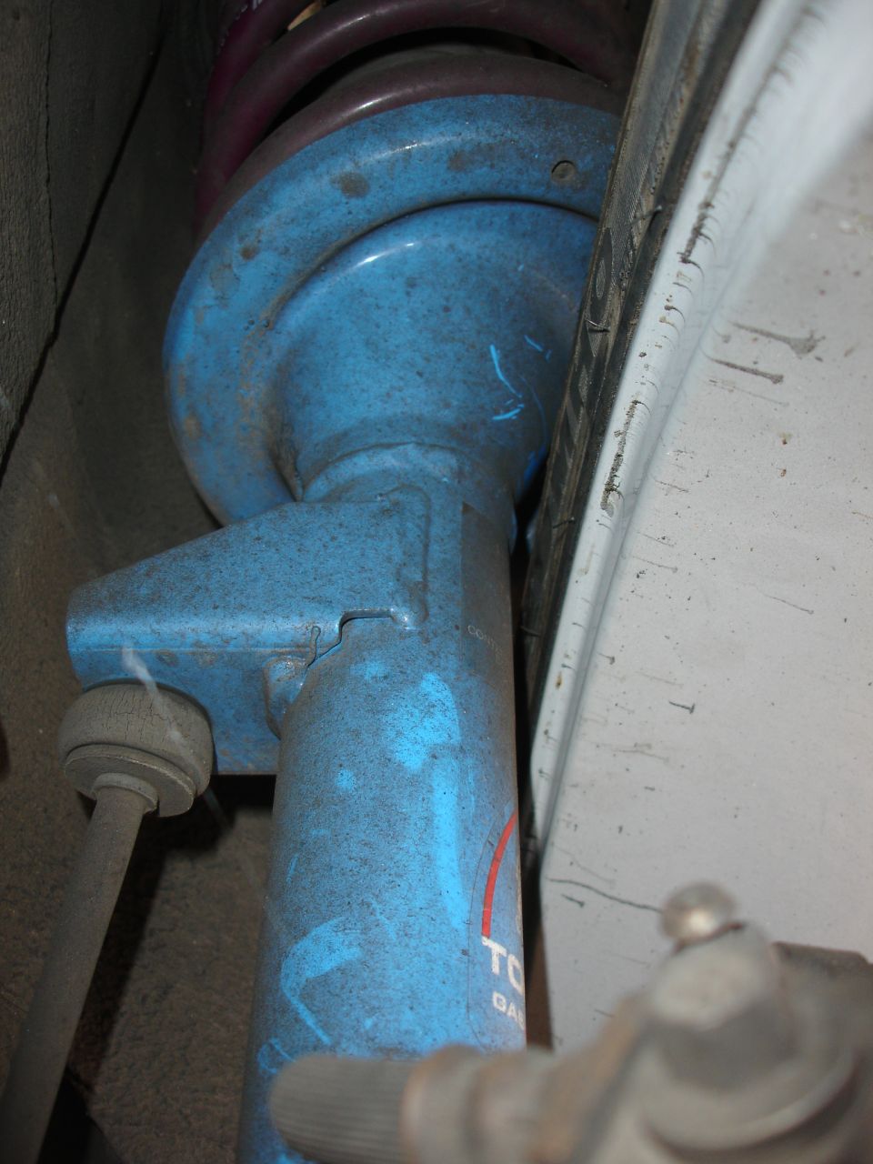 Blue shock absorber with partial red and white lettering, showing a purple spring and part of a tire