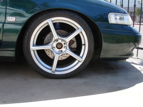 1993 Ford Taurus - Close-up of a green car's front wheel, showing custom rims and brake details. A "24V DOHC" badge is visible on the fender.