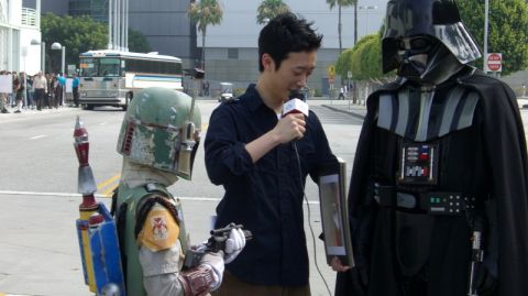 1990 Ford Probe - Cosplayers dressed as Boba Fett and Darth Vader are interviewed by a reporter on a city street.