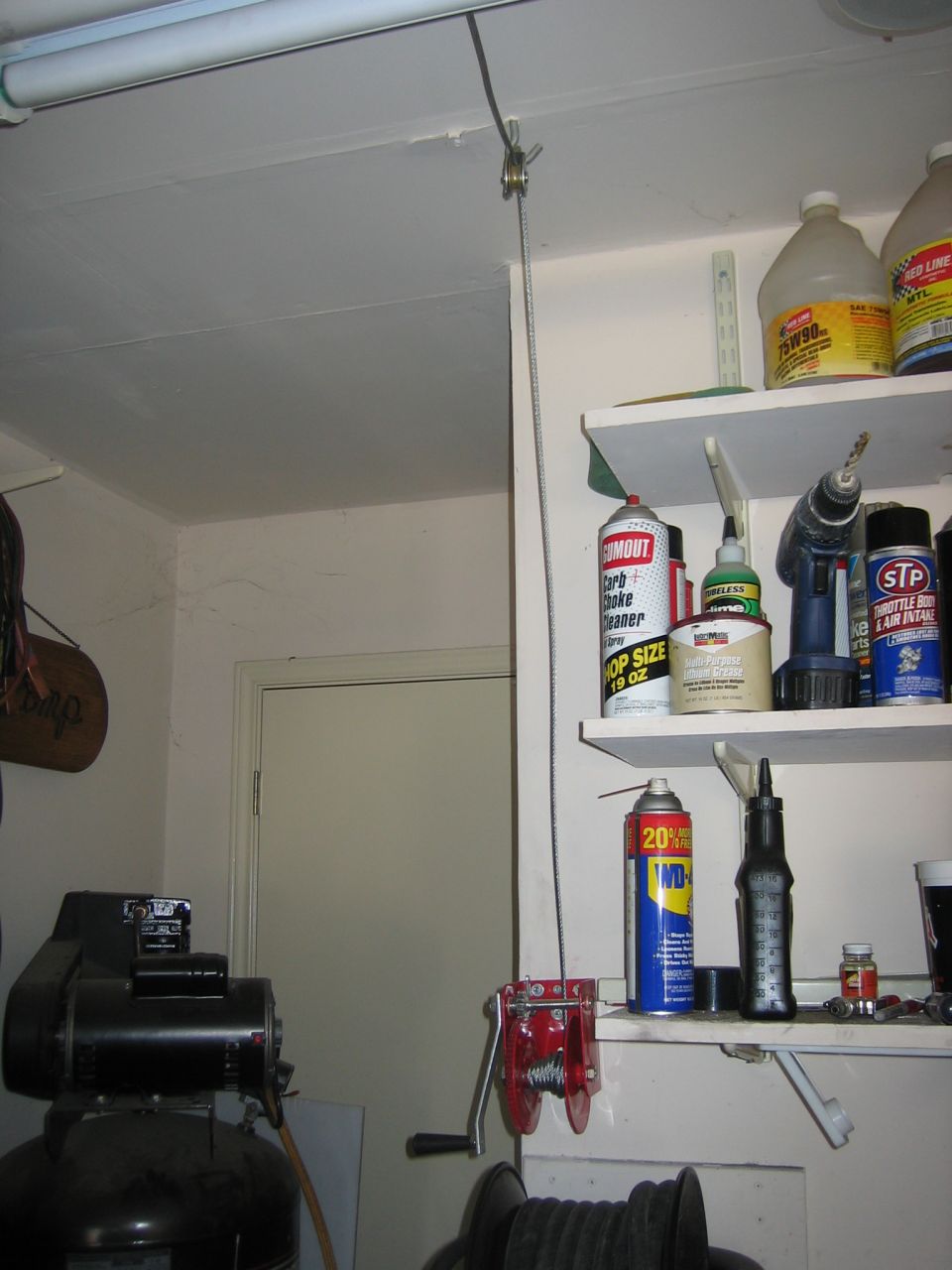 Garage interior with a hoist mechanism, shelves stocked with automotive fluids and tools, and an air compressor