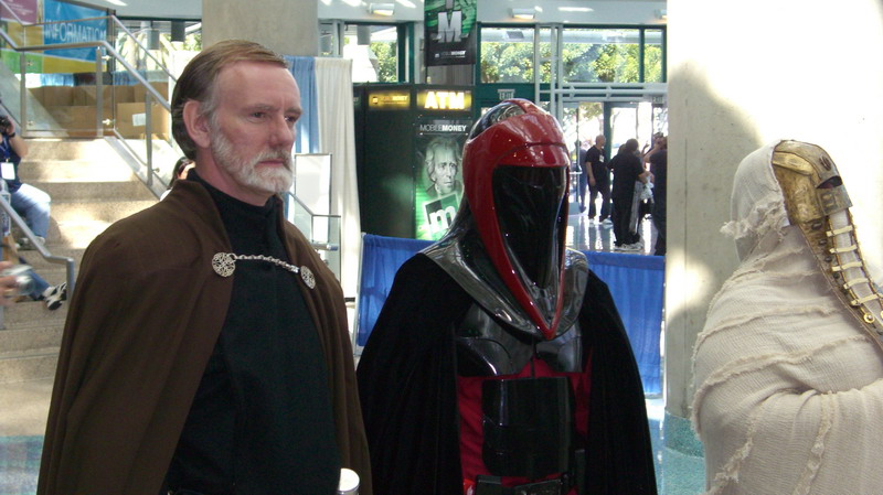 Three people in costumes, one with a brown cape, one in red armor, and one in mummy-like wrappings