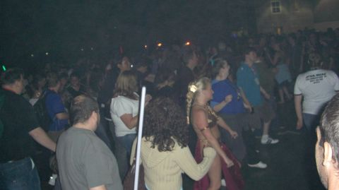 1990 Ford Probe - A large group of people are gathered outdoors at night, some dressed in costumes, dancing under artificial lights.