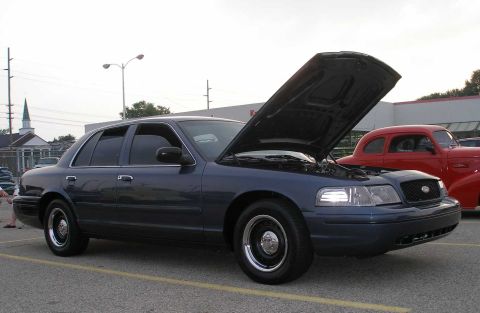 1998 Ford Crown Victoria - A 1998 Ford Crown Victoria is parked with its hood open, alongside a red classic car.