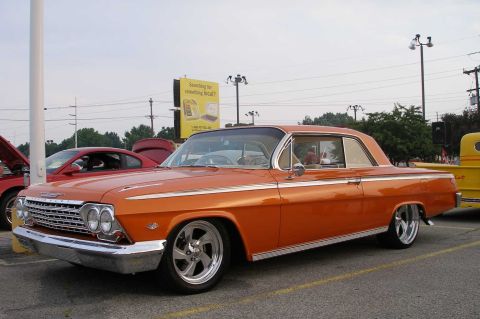 1998 Ford Crown Victoria - A classic orange Chevrolet Impala is parked in a lot, with other vehicles visible in the background.
