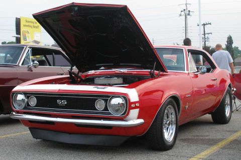 1998 Ford Crown Victoria - A red 1967 Chevrolet Camaro SS is parked with its hood open, next to another vehicle.