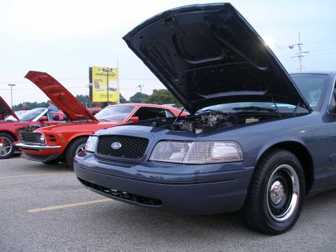 1998 Ford Crown Victoria - A dark blue Ford Crown Victoria is parked with its hood open, alongside other vehicles.