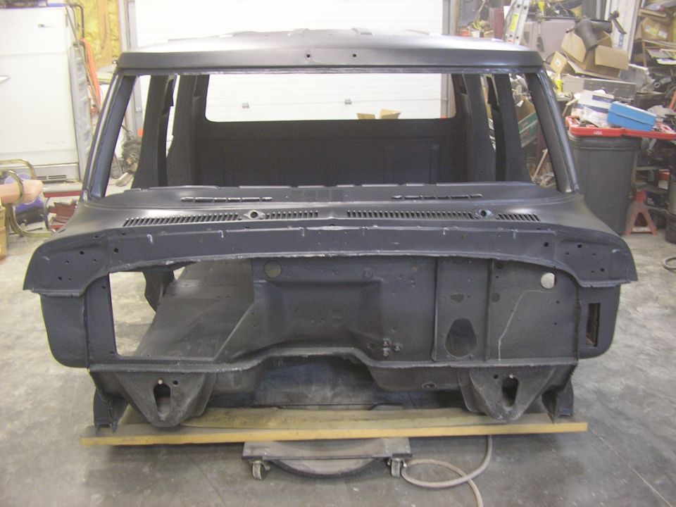 Stripped truck cab in dark primer showing firewall and cowl, on wood planks in a garage.