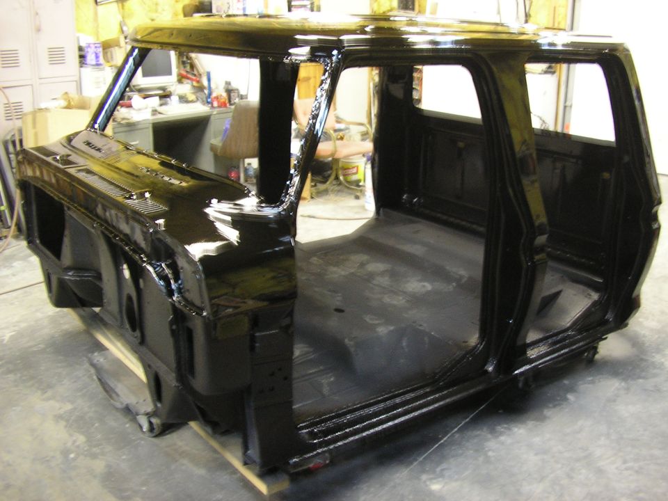 Freshly painted black truck cab shell on stands in a workshop, doors and glass removed.