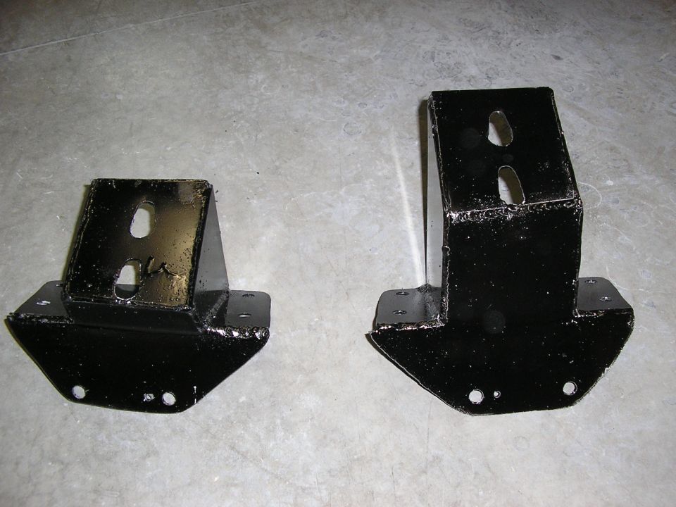 Two black welded steel mounting brackets with slotted holes on concrete floor