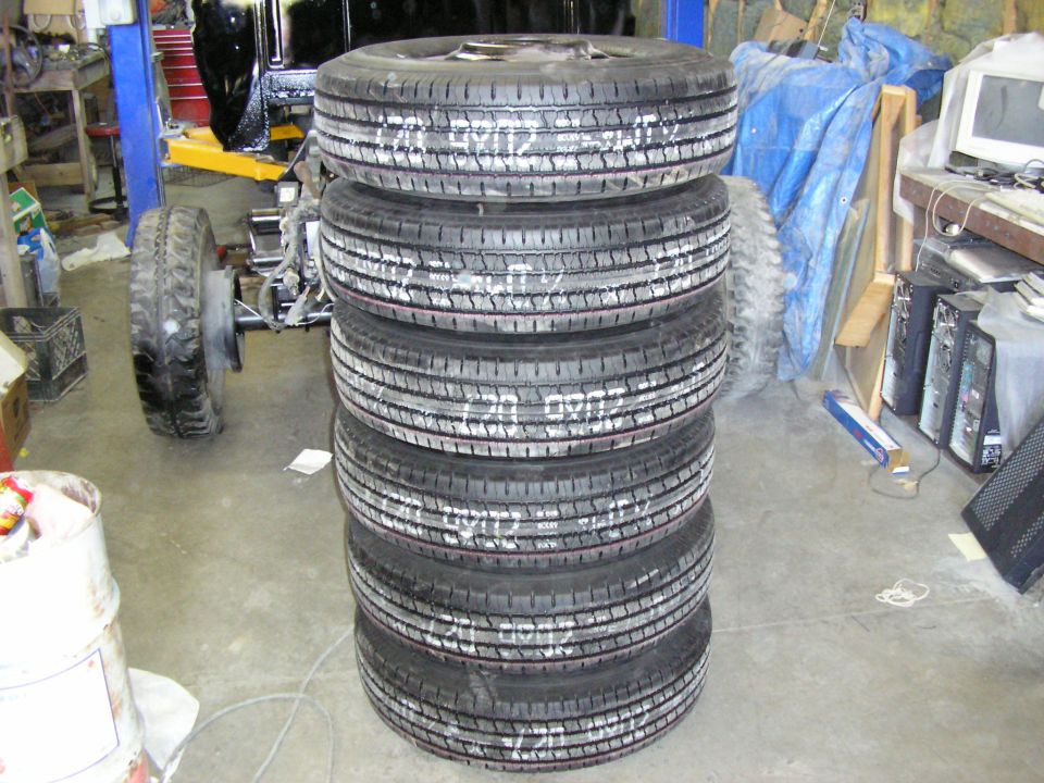 Stack of six tires on wheels marked '720 9902' in a cluttered garage