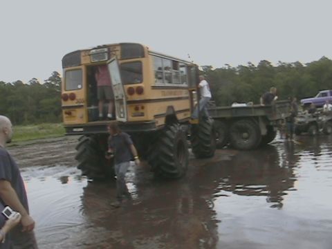 1976 Chevrolet Blazer - A heavily modified school bus with oversized tires navigates through a muddy, watery terrain, with other vehicles present.