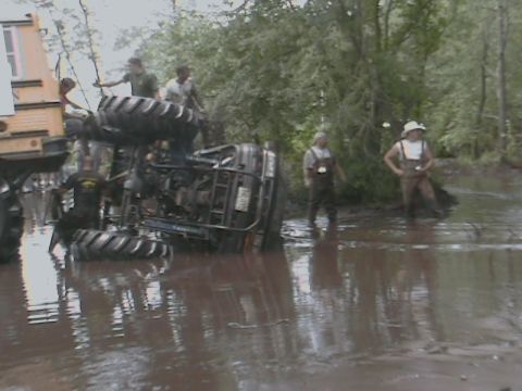 1976 Chevrolet Blazer - An ATV is overturned in the mud with several people standing nearby and a portion of a yellow vehicle visible.