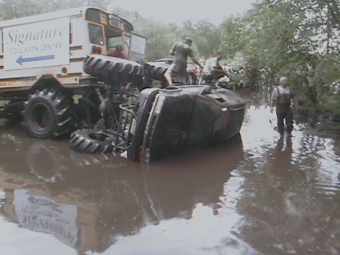 1976 Chevrolet Blazer - An overturned vehicle rests in the mud next to a large truck, with several people observing the scene.
