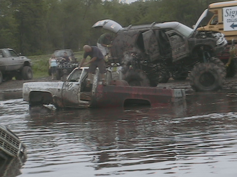 Muddy scene with a white and red pickup truck partially submerged, other off-road vehicles in background