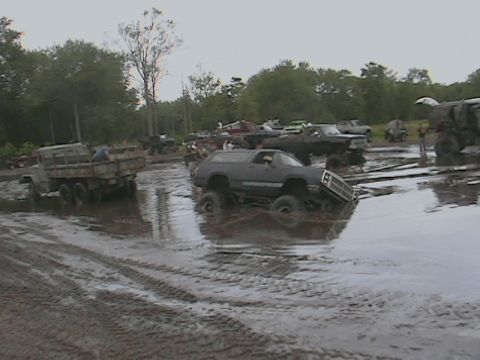 1976 Chevrolet Blazer - Several vehicles are seen in a muddy area, with one dark SUV prominently stuck in the mire.