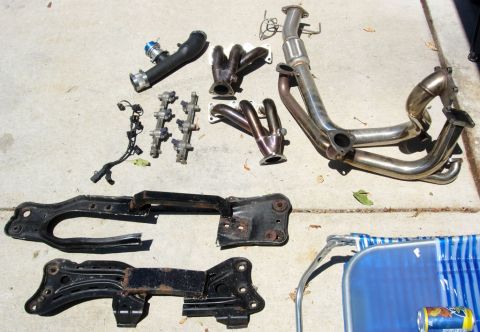 1994 Ford Probe - Various automotive engine and chassis parts are displayed on a concrete surface, including exhaust and intake components.