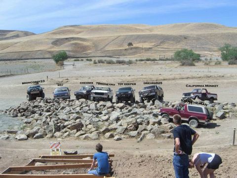 1989 Ford Bronco - Several off-road vehicles, including a red 1989 Ford Bronco, are parked on a rocky incline under a clear sky.