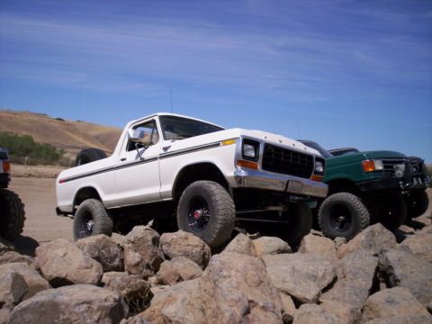 1989 Ford Bronco - Two Ford Broncos navigate a rocky terrain under a clear blue sky.