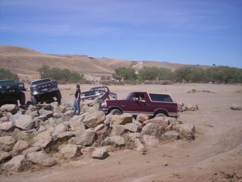 1989 Ford Bronco - Several trucks, including a 1989 Ford Bronco, are off-roading over a rocky obstacle course.