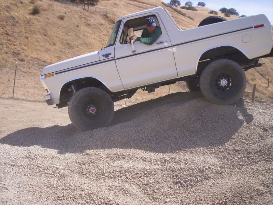White Ford Bronco climbing a gravel hill, driver visible