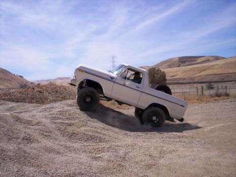 1989 Ford Bronco - A white Ford Bronco navigates a steep gravel incline under a partly cloudy sky.