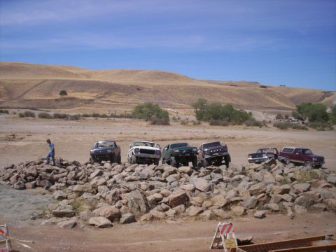 1989 Ford Bronco - Multiple trucks and SUVs are positioned on a large pile of rocks under a clear blue sky.