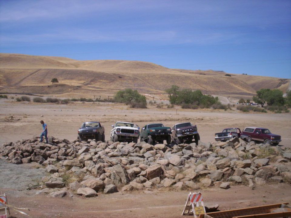 Several off-road trucks and SUVs parked on a rocky incline with a person standing nearby