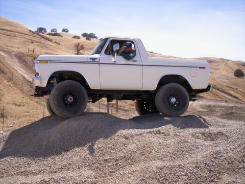 1989 Ford Bronco - This lifted Ford Bronco is navigating a rocky incline under a clear blue sky.