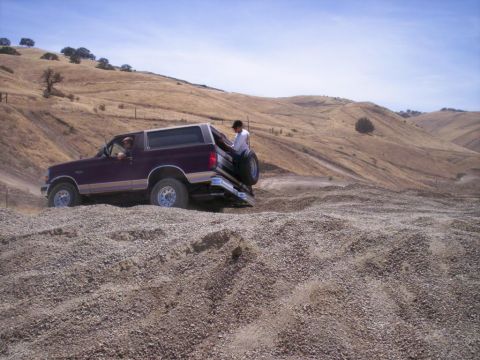 1989 Ford Bronco - A 1989 Ford Bronco navigates a steep, gravelly incline under a clear blue sky.