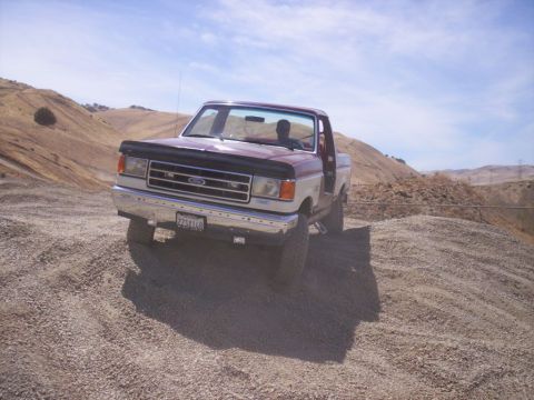 1989 Ford Bronco - This Ford F-150 pickup truck is parked on a gravelly incline under a clear blue sky.