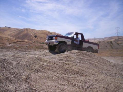 1989 Ford Bronco - A man drives a two-tone Ford pickup truck off-road on a sunny day.