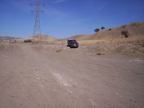 1989 Ford Bronco - A maroon Ford Bronco is parked on a dirt road, with rolling hills and a large power line tower under a clear blue sky.