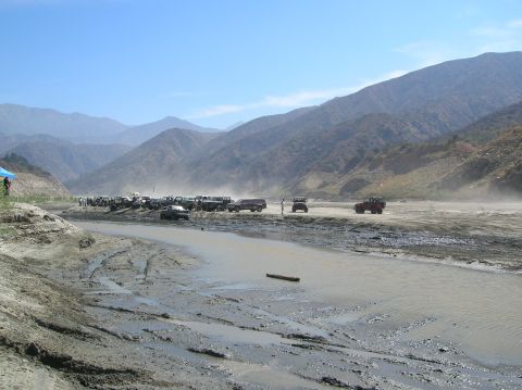 1985 Ford Bronco - A dry riverbed filled with various off-road vehicles under a clear blue sky.