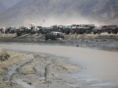 1985 Ford Bronco - Multiple off-road vehicles are gathered in a muddy, outdoor scene with hills in the background.