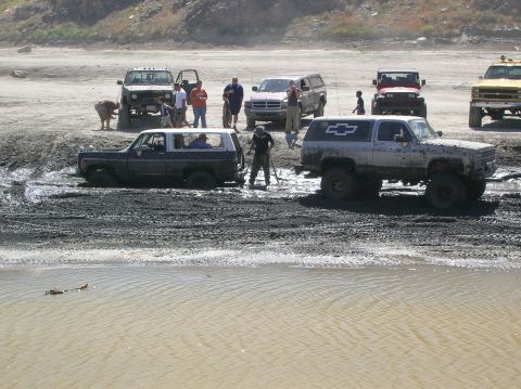 1985 Ford Bronco - Off-road vehicles are stuck in the mud while people stand around observing the situation.