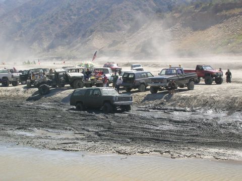 1985 Ford Bronco - Several off-road vehicles are parked on a dirt embankment, with dust kicked up in the air.