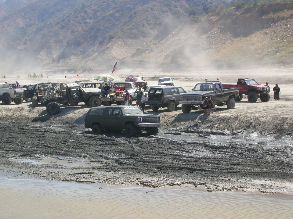Muddy off-road vehicles gathered on a dirt embankment with mountains in the background