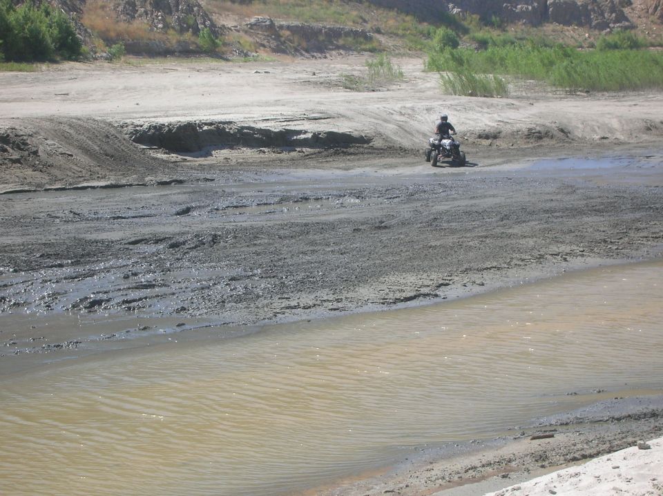ATV rider on dirt path near water, with sandy hills in background